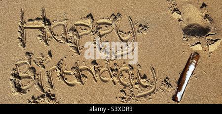 Joyeux anniversaire écrit dans le sable avec une coquille de rasoir. Banque D'Images