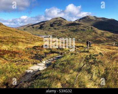 Marcheurs sur le chemin en direction de la crête de Tarmachan avec une vue sur la chaîne de montagnes Ben Lawers, et le barrage de Lawers, à Killin, en Écosse Banque D'Images