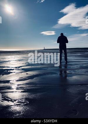 Homme rétroéclairé debout sur une plage à marée basse Banque D'Images