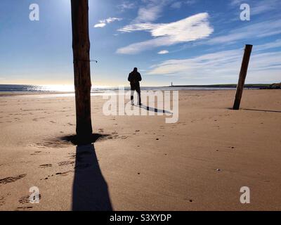 Homme rétroéclairé debout sur une plage à marée basse Banque D'Images