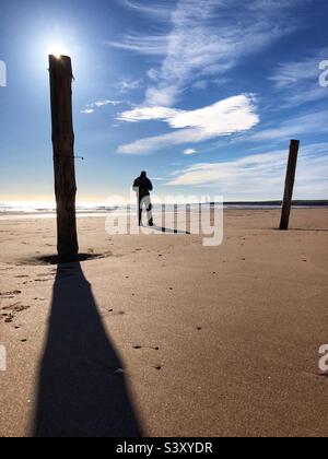 Homme rétroéclairé debout sur une plage à marée basse Banque D'Images