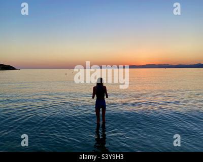 Fille en silhouette pagayant dans la baie de Lardos au coucher du soleil. Pefkos sur l'île de Rhodes, Grèce Banque D'Images