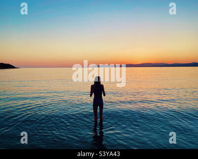 Coucher de soleil à Pefkos sur l'île de Rhodes, Grèce. Fille en silhouette pagayant en mer au crépuscule. Banque D'Images