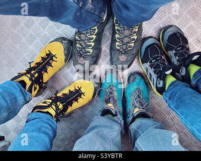 Quatre paires de jambes et pieds en bottes de randonnée POV sur le plancher métallique d'un ascenseur de cabine : une famille sur le chemin du retour d'une randonnée Banque D'Images