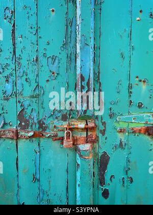 Vieux cadenas rouillé sur une porte bleu sarcelle avec peinture écaillée. Banque D'Images
