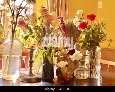 Belle maison de cuisine tabescape avec fleurs coupées dans une variété de pots en verre et vases en céramique avec chandelier décoratif dans la cuisine de campagne jaune vif au printemps, Angleterre Banque D'Images