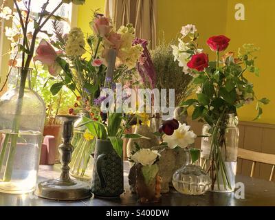 Groupe de fleurs coupées dans des vases en verre et en céramique, des cruches et des bocaux sur une table de cuisine de chalet de campagne anglaise Banque D'Images