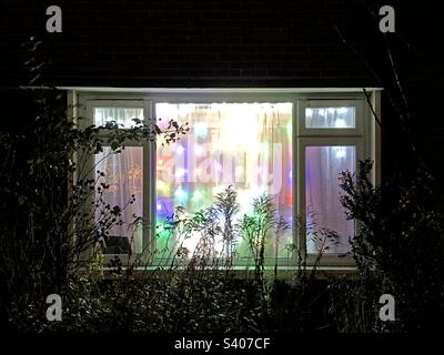 Une fenêtre de salon vue de l'extérieur avec des lumières de Noël colorées. Banque D'Images
