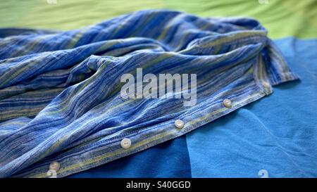 Boutons blancs dirigés vers l'avant sur une chemise en lin bleu, vert et indigo placée sur une couverture de lit bleu, vert et indigo, créant une image abstraite, adaptée à l'arrière-plan graphique Banque D'Images