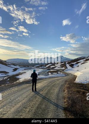 Fille debout et regardant le paysage de montagne sur une route de gravier de montagne dans Nordland, nord de la Norvège, au printemps, juin, dans une soirée ensoleillée. Banque D'Images