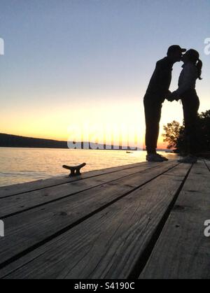 Couple heureux embrassant sur le quai silhoueté par le coucher de soleil stupéfiant sur le lac Skaneateles. Banque D'Images