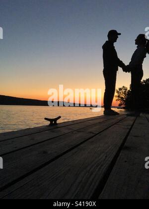 Silhouette de couple tenant les mains sur le quai à bateaux avec un magnifique coucher de soleil sur le lac Skaneateles. Banque D'Images