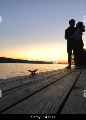 Silhouette de couple heureux enchâssant sur le quai à bateaux avec un magnifique coucher de soleil sur le lac Skaneateles. Banque D'Images