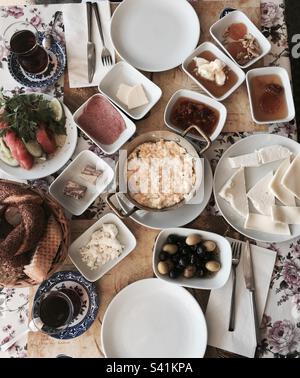 Petit déjeuner turc avec œufs brouillés, olives, salami, fromage, miel et crème, Simit, confiture, thé turc, pain, halva, Tomate, concombre, persil, beurre, coutellerie et deux assiettes à Galata Istanbul Banque D'Images