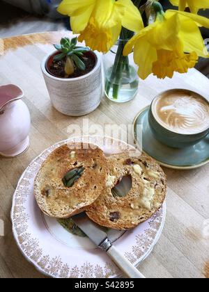 Un café blanc plat et un bagel à la cannelle grillé sur une table avec des jonquilles Banque D'Images