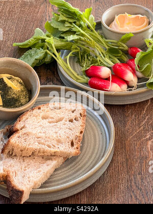 Les radis et une trempette sur une assiette et le pain frais coupé en tranches avec du beurre sur une autre table Banque D'Images