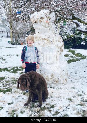 Garçon de six ans avec son chien de labradoodle dans la neige. Hampshire, Angleterre, Royaume-Uni. Banque D'Images