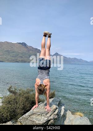 Une femme athlétique qui fait un stand au lac Wakatipu sur la péninsule de Kelvin Heights près de Queenstown, dans l'île du Sud de la Nouvelle-Zélande Banque D'Images