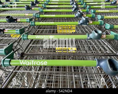 Les manches de longues lignes de chariots de supermarché vides, attendant à l'extérieur du magasin et portant le logo Waitrose. Banque D'Images