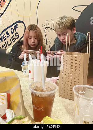 Jeune couple asiatique sur les téléphones cellulaires au McDonalds. Banque D'Images