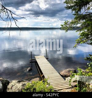 Pendant un été arctique, on couve des nuages de tempête sombres qui se reflètent dans un grand lac, sur un quai d'été dans la région de Kajaani en Finlande Banque D'Images