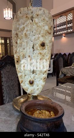 Pain naan afghan géant servi avec du curry de poulet dans un pot en argile Banque D'Images