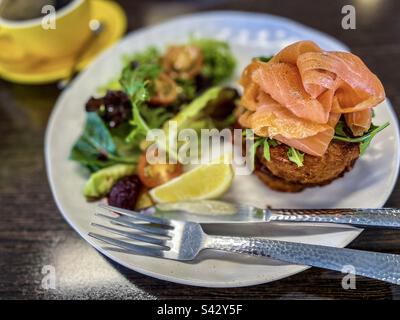 Saumon fumé sur des pancakes aux pommes de terre avec salade fraîche sur l'assiette et une tasse de café sur la table. Banque D'Images