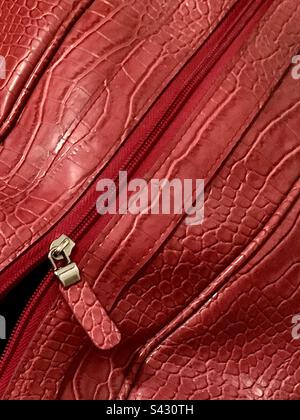 Gros plan sur un sac de sport en cuir rouge à la texture peau de serpent, fermeture à glissière partiellement ouverte dans le coin inférieur Banque D'Images
