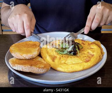 Section médiane de l'homme en utilisant des couverts pour couper l'omelette au fromage veggie sur l'assiette avec du pain au levain. Banque D'Images