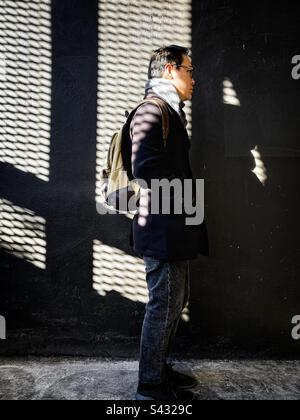 Vue latérale complète d'un jeune homme debout contre un mur à motifs ombrés. Banque D'Images