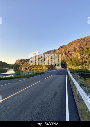 Route asphaltée de montagne allant dans le tunnel dans les îles Lofoten, en Norvège, lors d'une nuit ensoleillée d'été. Banque D'Images