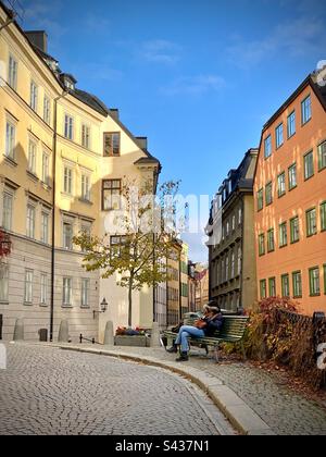 Une femme assise lisant sur une place calme parmi les magnifiques extérieurs peints orange et jaune ombragée de bâtiments traditionnels dans les rues étroites de la vieille ville de Stockholm Gamla Stan en Suède Banque D'Images