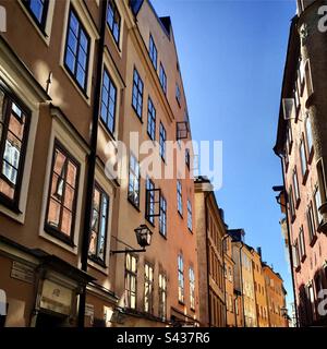 Les magnifiques extérieurs peints orange et jaune ombrageux des bâtiments traditionnels sur les rues étroites de la vieille ville de Stockholm Gamla Stan en Suède sous un ciel bleu clair Banque D'Images