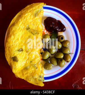 La moitié d'une tortilla espagnole avec des œufs, des pommes de terre et des oignons, des olives et un piment rouge chaud au Mexique Banque D'Images