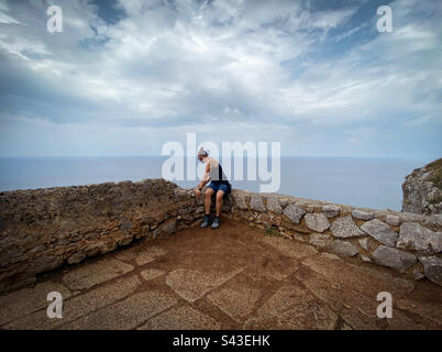 Homme assis sur un mur de pierre, regardant la falaise. Banque D'Images