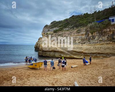 Groupe de personnes debout près d'un bateau jaune sur la plage de Benagil en Algarve, Portugal. Banque D'Images