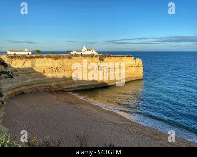 Vue sur le coucher du soleil à l'église blanche sur les falaises de grès Senhora da Rocha et la plage de Praia Nova en Algarve, Portugal. Banque D'Images