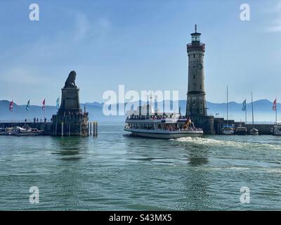 Ferry en bateau sortant du port de Lindau entre la statue du lion et le phare sur le lac Bodensee avec vue sur les montagnes, Allemagne. Banque D'Images