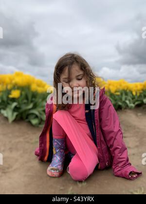 Petite fille assise dans le champ de tulipes jaunes. Banque D'Images