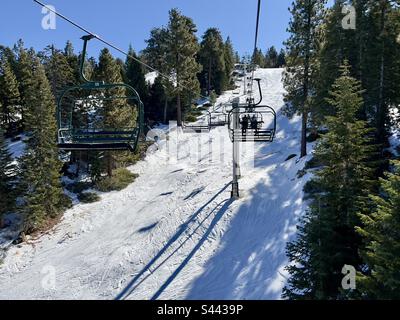 Vue arrière des skieurs et snowboardeurs non identifiés sur le télésiège en remontant la montagne enneigée, à côté des pins, à Big Bear, Californie Banque D'Images