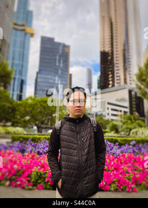 Le printemps fleurit dans la ville. Jeune homme asiatique debout devant des massifs de fleurs colorés contre des arbres, des bâtiments et le ciel à Melbourne, Victoria, Australie. Banque D'Images