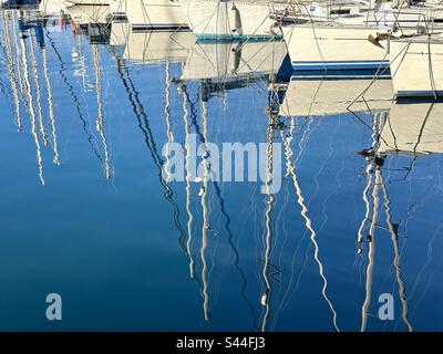 Les mâts de bateaux à voile se reflètent dans l'eau bleue lors d'une journée ensoleillée Banque D'Images