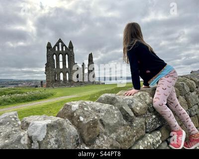 Abbaye de Whitby avec vue arrière d'une fille grimpant sur le mur de pierre pour voir Banque D'Images