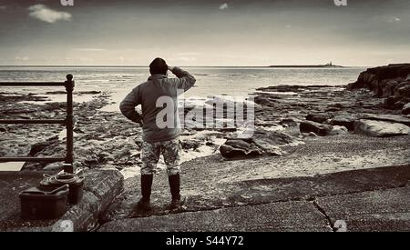 Un pêcheur donne sur l'île de Coquet depuis la côte de la ruée par une journée claire dans le Northumberland. (Noir et blanc) Banque D'Images