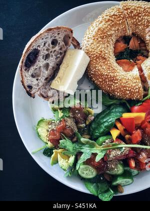 Directement au-dessus de la vue de bagel de saumon, levain d'olive avec fromage et salade fraîche, tranches d'avocat sur plaque blanche sur table noire. Mangez vos couleurs. Une alimentation saine. Banque D'Images