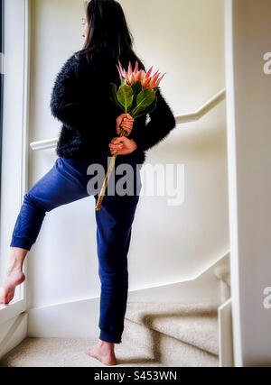 Vue sur toute la longueur de la jeune femme asiatique tenant un roi protea également connu sous le nom de fleurs de protea cynaroides derrière son dos sur l'escalier. Banque D'Images