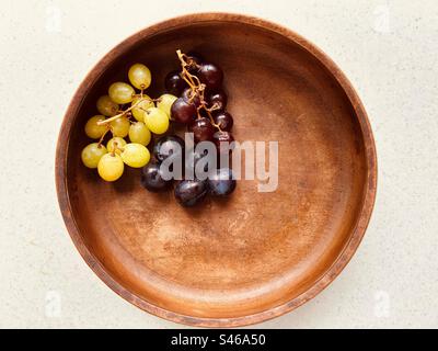 Prunes et raisins dans un bol circulaire en bois. Deux grappes. Raisins rouges, raisins verts. Prunes bleues violacées. frais et juteux. Banque D'Images