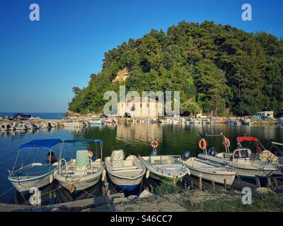 Vieux port avec des bateaux au coucher du soleil avec colline verte en arrière-plan à Skala Potamias, île de Thassos, Grèce. Banque D'Images