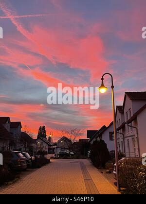 Sous les teintes rosées d'un coucher de soleil, un lampadaire projette sa lueur chaude, marquant la transition du jour à la nuit dans une scène urbaine tranquille. Banque D'Images