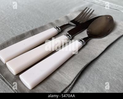 Couverts à manche blanc (couteau, fourchette et cuillère) sur des serviettes vertes avec une nappe verte Banque D'Images